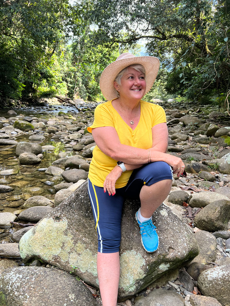 Sue sitting on a rock by a stream.
